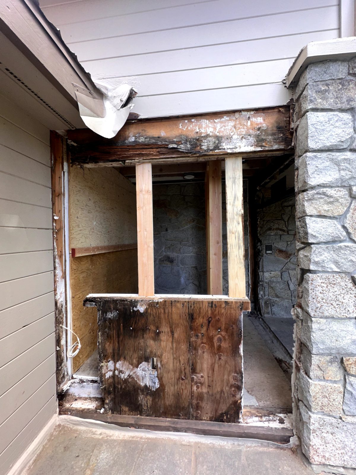 Rotted deck framing and siding under a stone archway before restoration